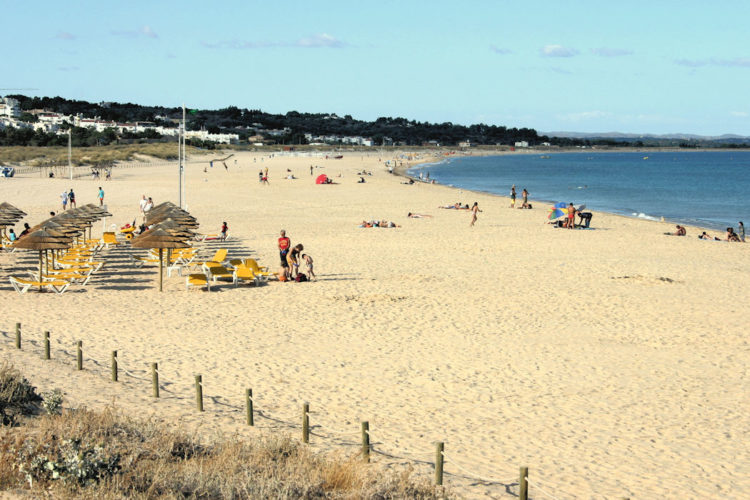 The long, sweeping beach of Meia Praia shows a quiet scene of very few people despite blue skies and a calm sea