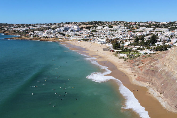 An aerial shot of Praia da Luz beach showing the sandy beach and surfers in the sea getting ready to catch the next wave